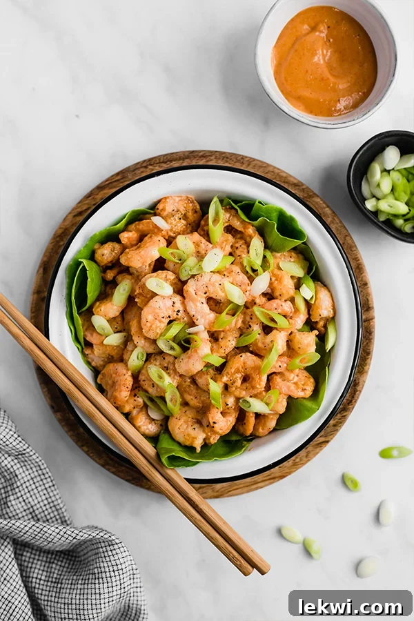 A close-up shot of crispy, golden Bang Bang Shrimp resting in a pan, coated in its signature creamy sauce, with a garnish of fresh herbs.