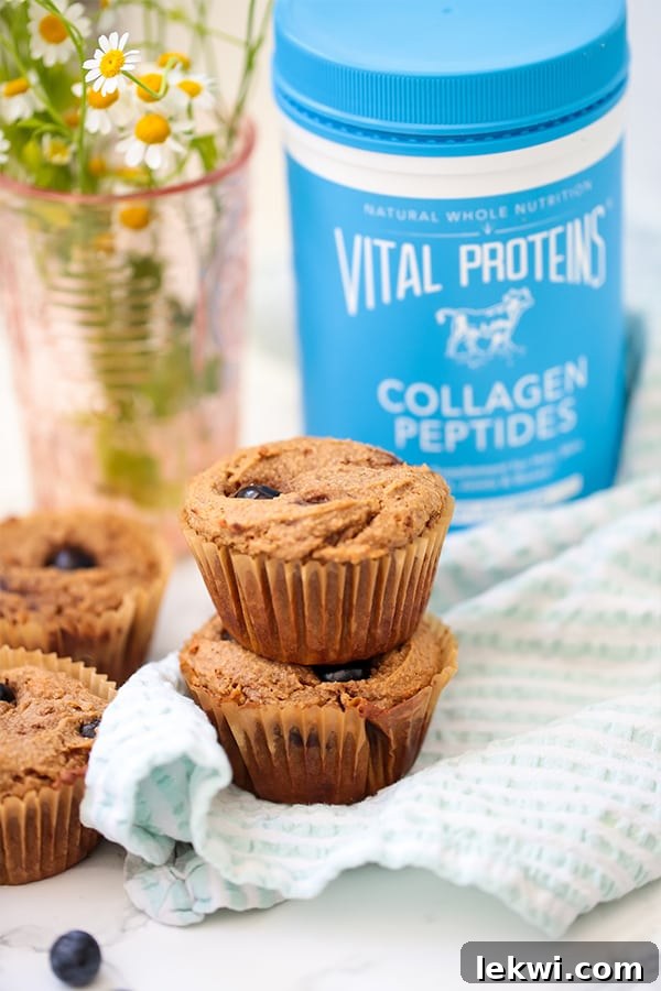 A stack of golden-brown blueberry banana muffins with fresh blueberries, resting beside a container of Vital Proteins Collagen Peptides, highlighting the healthy and delicious nature of the treat.