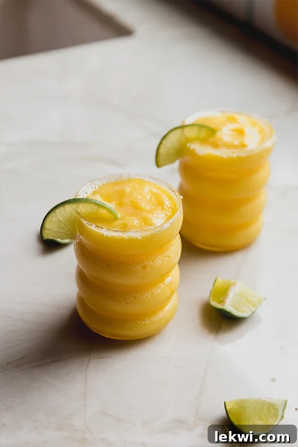 Two glasses of frozen mango margarita mocktail with lime slices, garnished with salt rims.