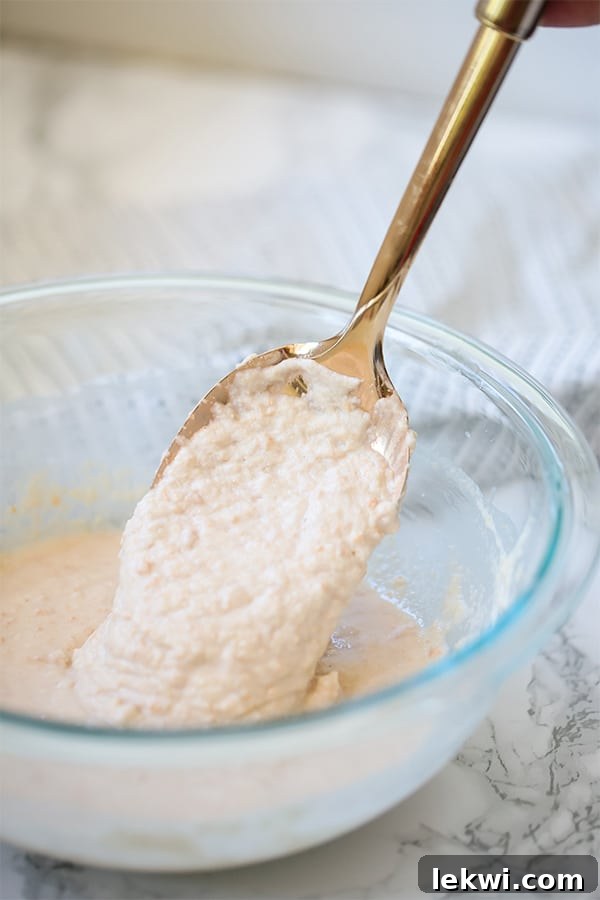 A bowl of thick pancake batter with a spoon mixing it, showing its smooth consistency