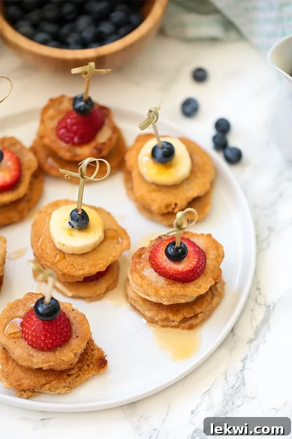 A beautifully arranged white plate showcasing mini pancake skewers with a variety of fresh fruits like strawberries, bananas, and blueberries