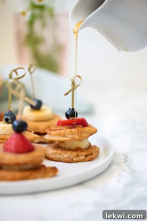 A white plate with mini pancakes on skewers with fresh fruit.