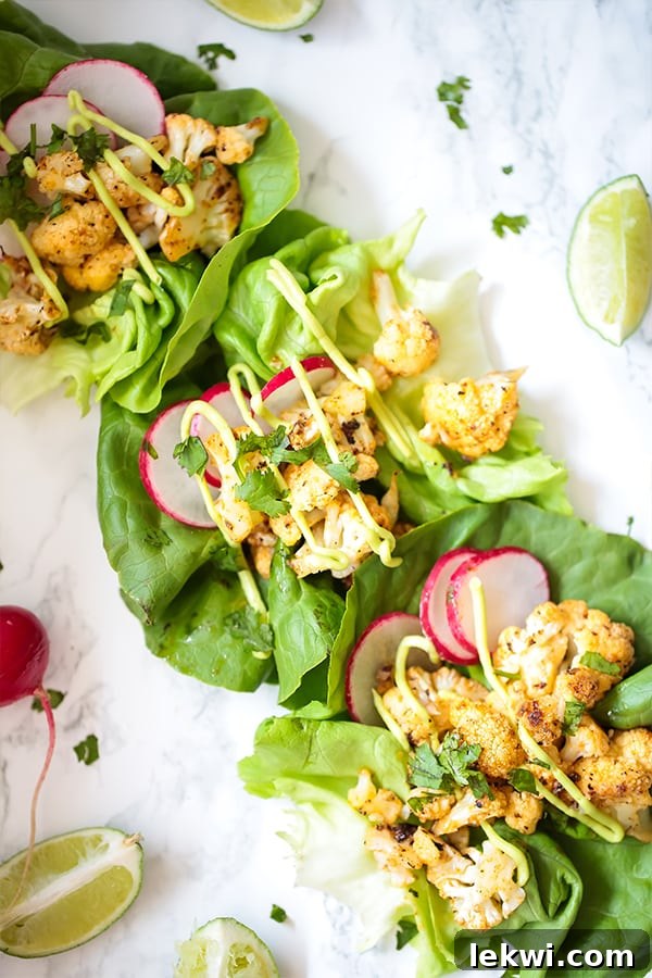 Three bang bang cauliflower tacos with lettuce on a counter with a slice of lime nearby.