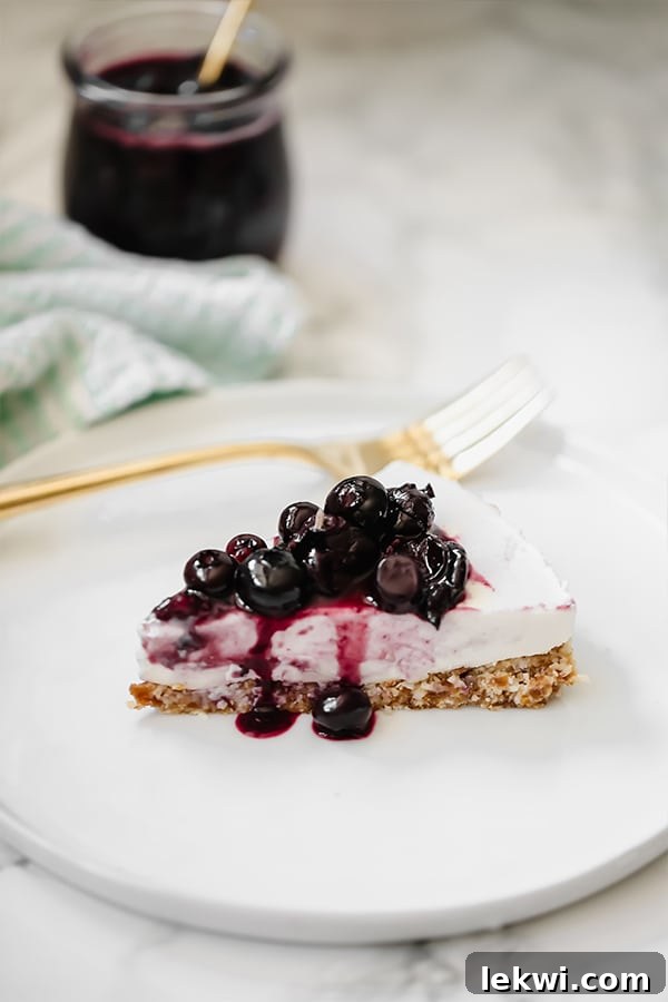 A perfectly sliced no-bake blueberry lavender cheesecake, adorned with fresh blueberries, resting on a pristine white plate beside a fork. The light purple filling contrasts beautifully with the dark blue topping.