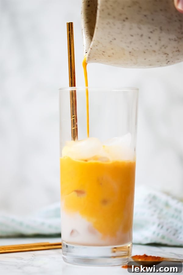 A close-up of a single glass of Iced Golden Milk Turmeric Latte, showing the rich golden color and a straw, set against a blurred background.