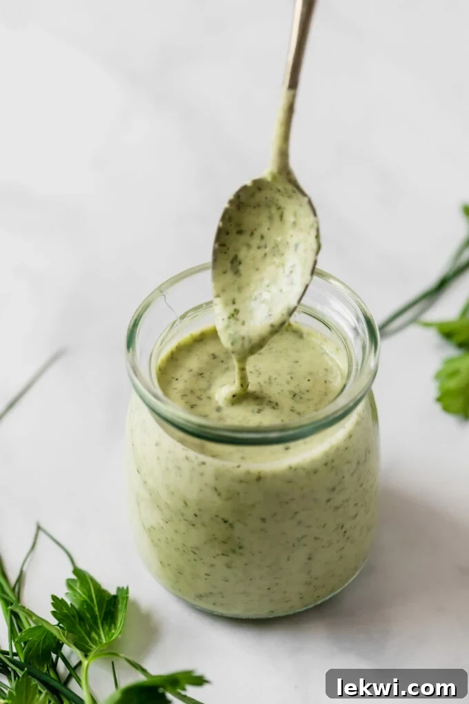 A glass jar of dressing for bacon ranch sweet potato salad with a spoon dipping into it.