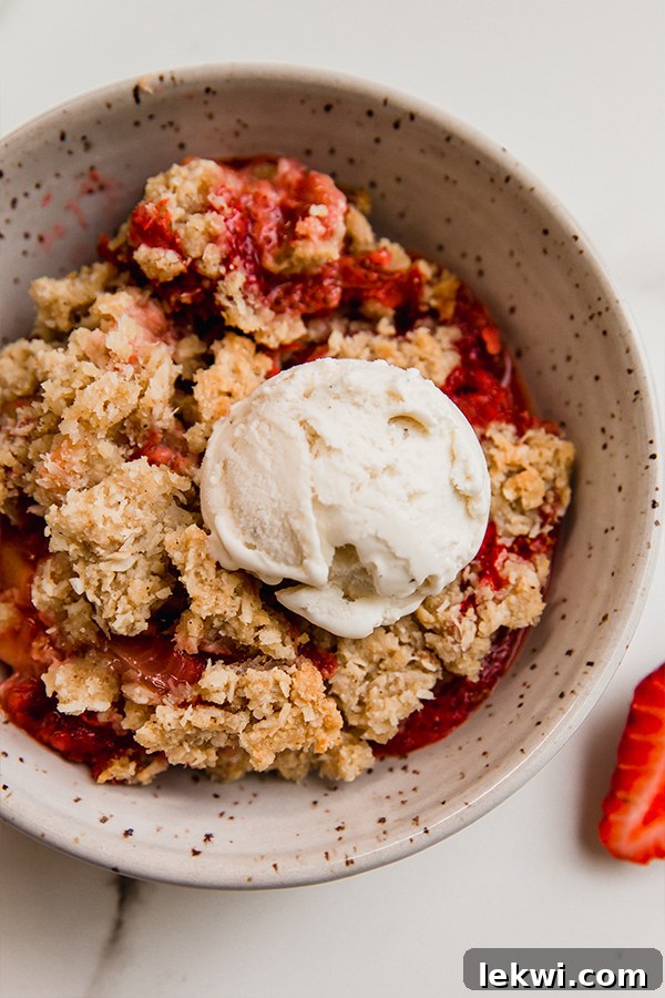 A close-up shot of a perfect serving of warm strawberry rhubarb crisp, exquisitely topped with a melting scoop of dairy-free vanilla ice cream, creating a delightful contrast of temperatures and textures for ultimate enjoyment.