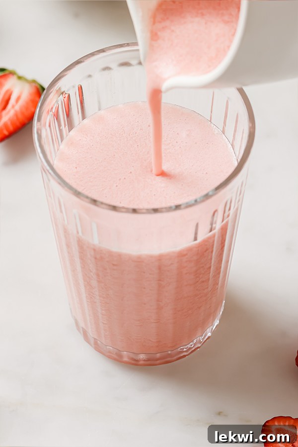 Creamy frozen pink lemonade pouring into a tall glass from a blender.