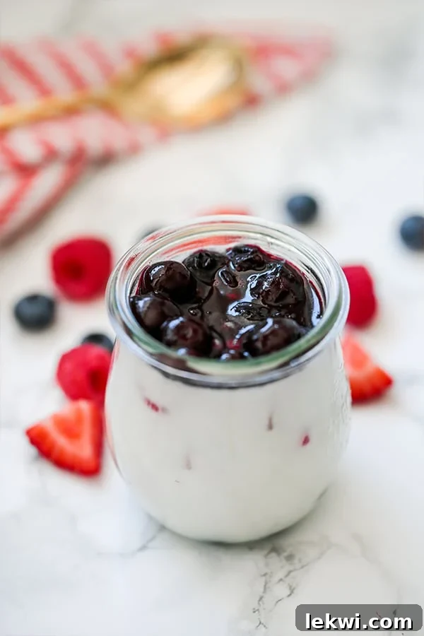 A glass jar filled with red, white, and blue panna cotta with fresh berries on a wooden counter beside it, ready to be enjoyed.