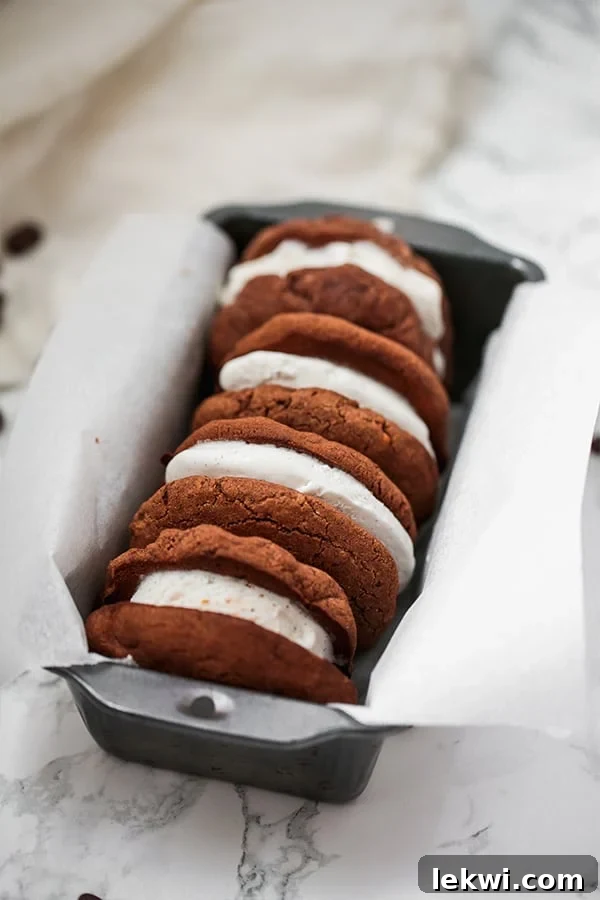 A trio of freshly made chocolate cookie ice cream sandwiches nestled in a loaf pan lined with parchment paper.