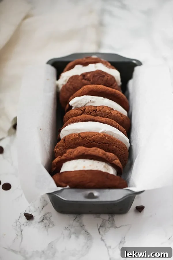 A neatly arranged stack of three homemade chocolate cookie ice cream sandwiches in a parchment-lined loaf pan, ready to serve.
