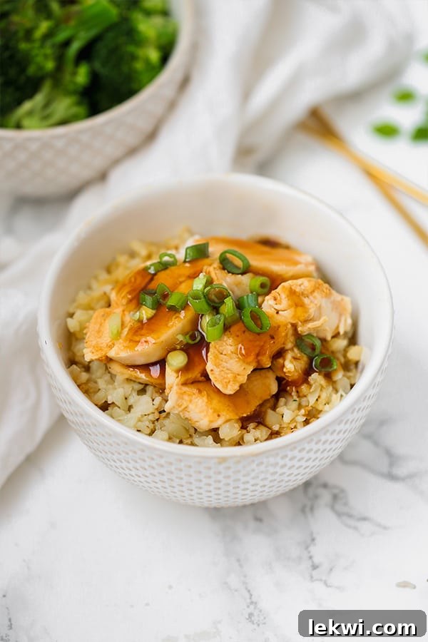 A white bowl with cauliflower rice topped with slow cooker chicken teriyaki, garnished with fresh green onion slices.