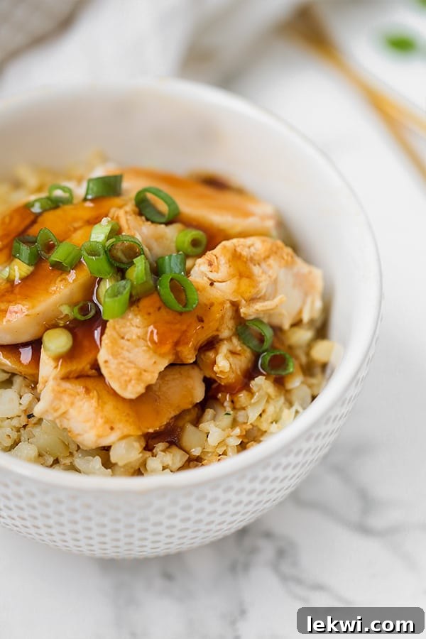 A bowl filled with chicken teriyaki on cauliflower rice topped with sliced green onions, ready to be served.