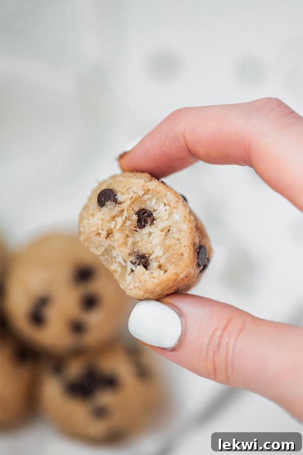 A hand gracefully holding a delicious cookie dough collagen protein bite, with a bite taken out, revealing its soft interior.