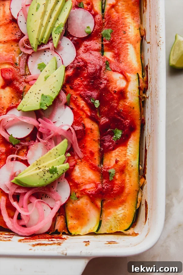 Zucchini enchilada casserole in a baking dish topped off with enchilada sauce, slices radish, avocado, pickled onion and cilantro.