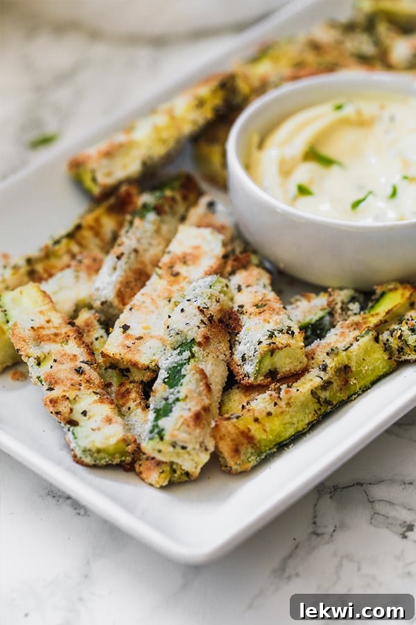 A vibrant platter of golden-brown zucchini fries elegantly arranged around a small white bowl of creamy dipping sauce, ready to be enjoyed.