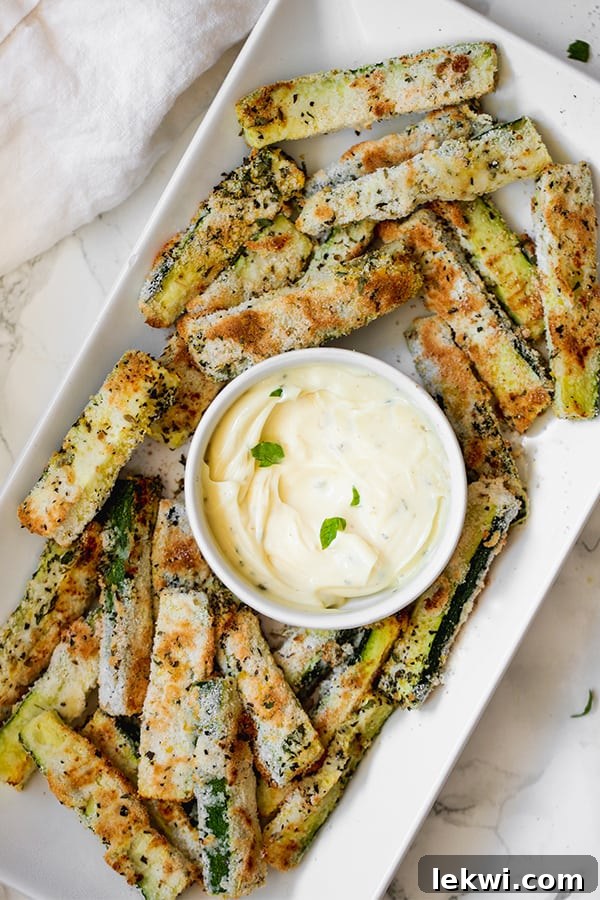 A white serving dish of zucchini fries around a white bowl of dipping sauce.