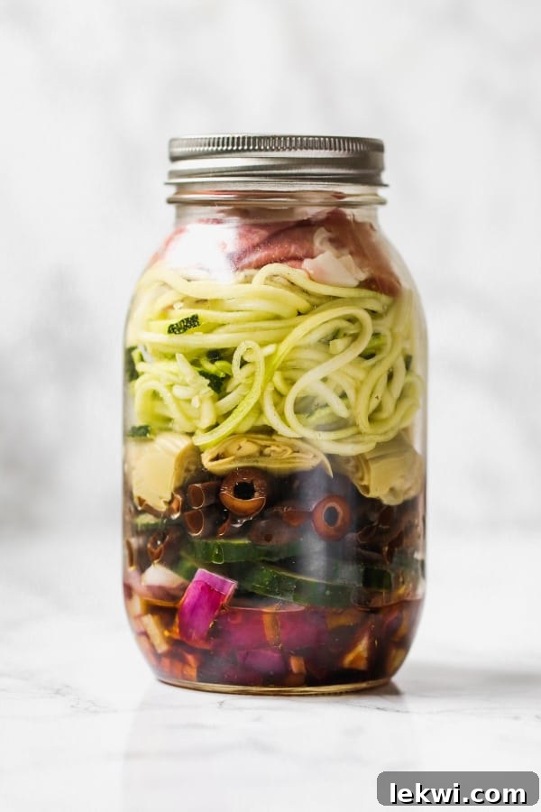 A mason jar filled with layers of onion, cucumber, olives, artichoke hearts, zucchini, and dressing.