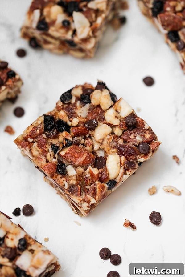 A single Paleo Grain-Free Granola Bar resting on a counter, surrounded by scattered almonds and chocolate chips, ready for a healthy snack.