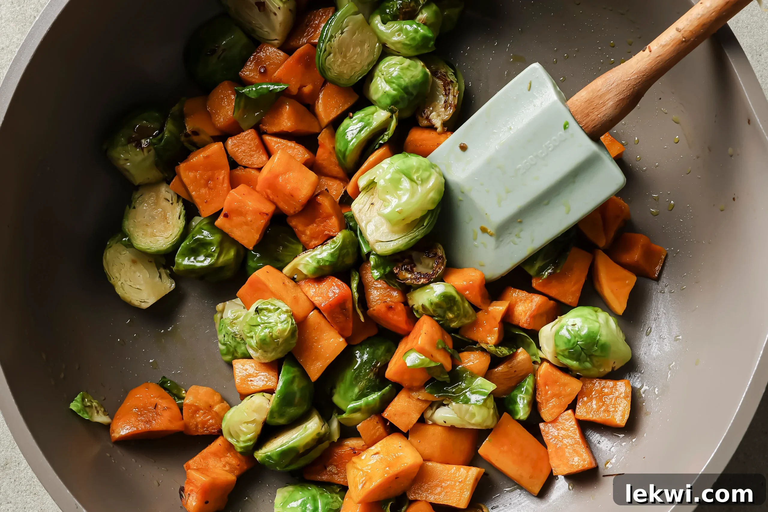 Diced sweet potatoes and brussels sprouts sautéing in a pan with oil.