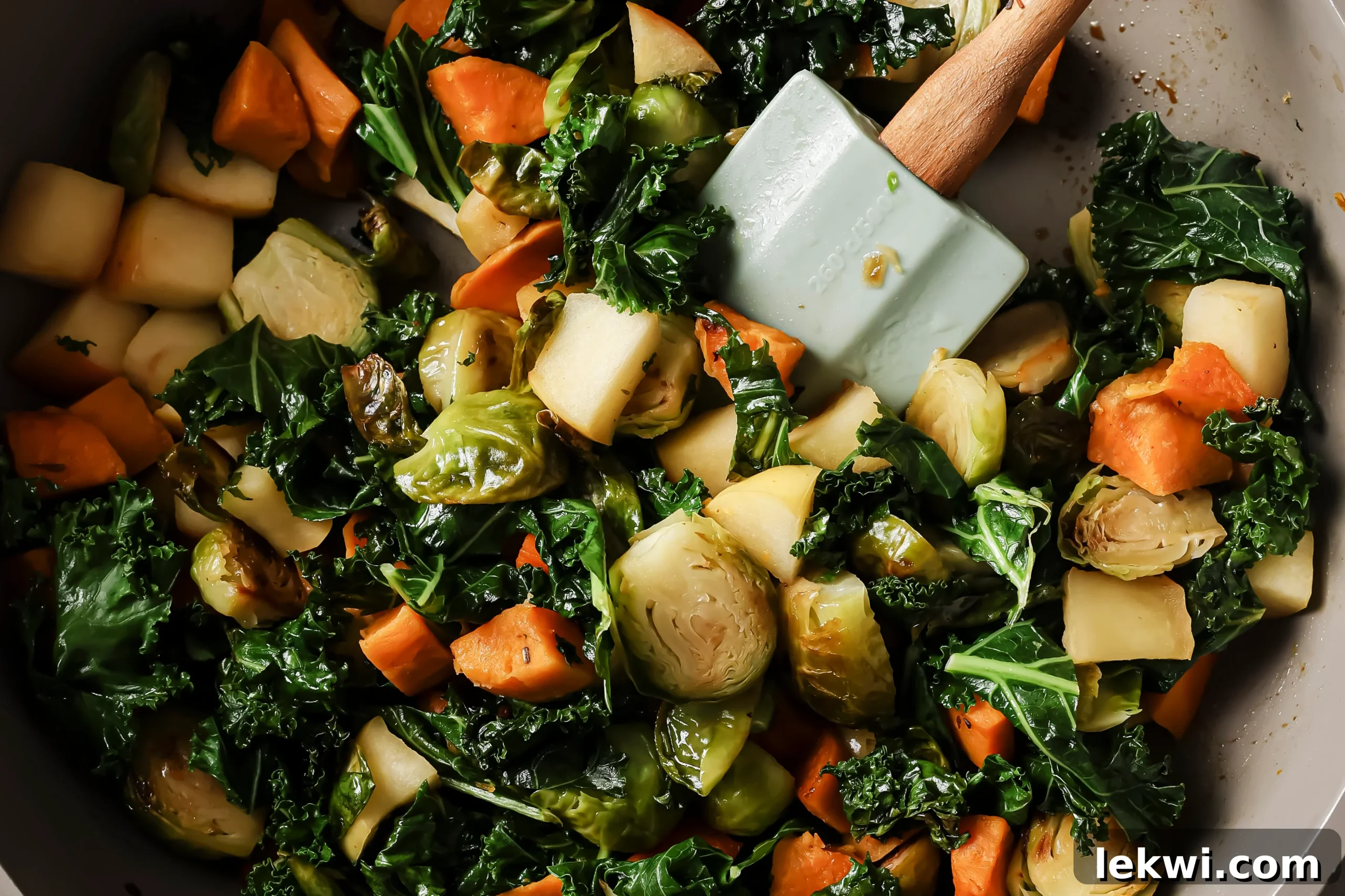 Kale and diced apples being added to the sautéed vegetables in the pan.