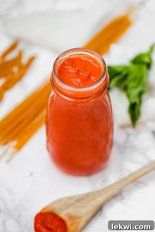 A glass jar filled with nightshade free marinara sauce with pieces of uncooked spaghetti lying next to it.