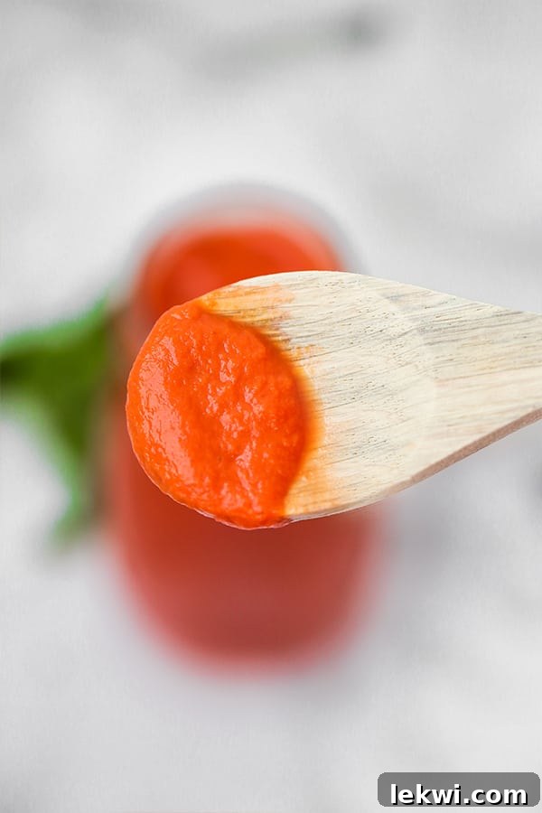 A wooden spoon taking a little bit of nightshade free marinara sauce out of the glass bottle of it.