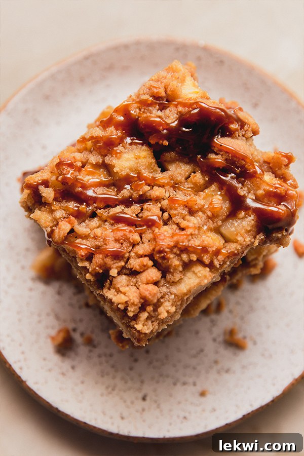 A single slice of paleo apple pie bar on a small white plate, showing the layers of apple filling and crumbly topping, ready to be enjoyed with a fork.