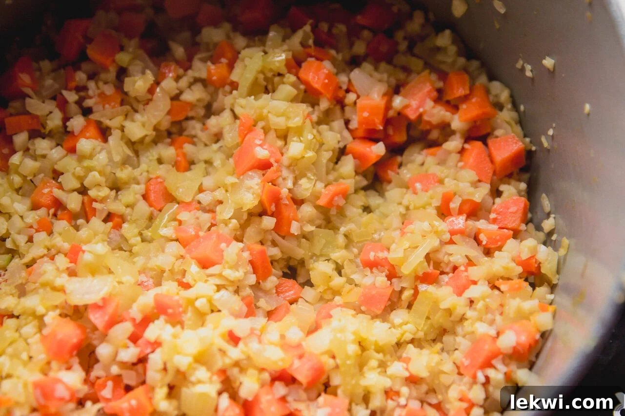 Diced carrots, celery, onion, and cauliflower rice sautéing in a large pot with olive oil.