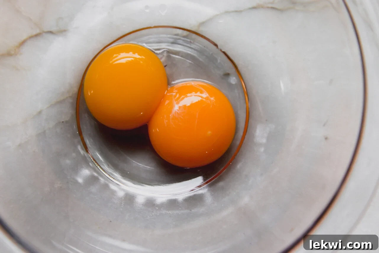 Three bright yellow egg yolks separated in a small glass bowl, ready for tempering.