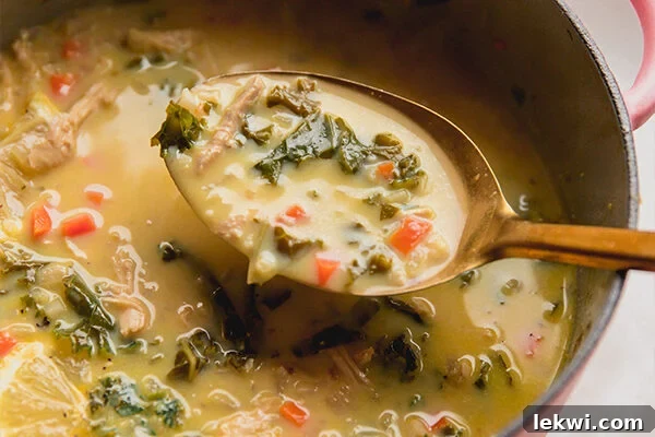A large ladle scooping a portion of rich Greek lemon chicken soup into a bowl, ready to be served.