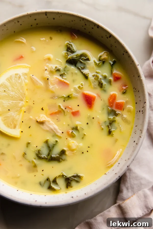 A bowl of Greek lemon chicken soup with a lemon slice on top, presented in a minimalist style.
