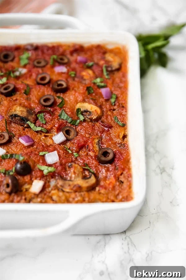 A white baking dish filled with spaghetti squash pizza casserole topped with olives, mushrooms, and onions.