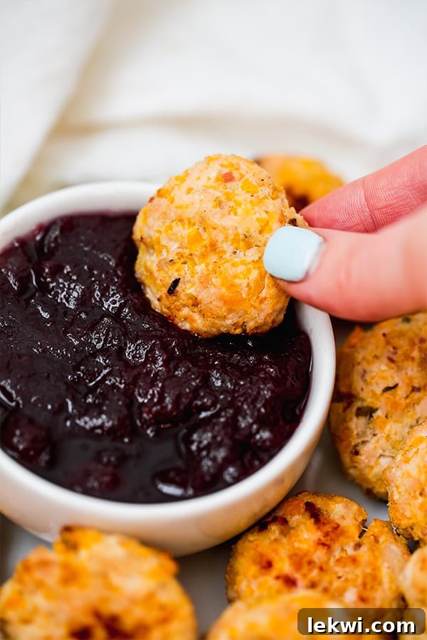 A hand dipping a butternut squash chicken popper into a small bowl of crimson dipping sauce.