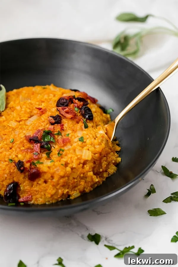 A black bowl filled with cauliflower pumpkin risotto with a spoon resting in it.