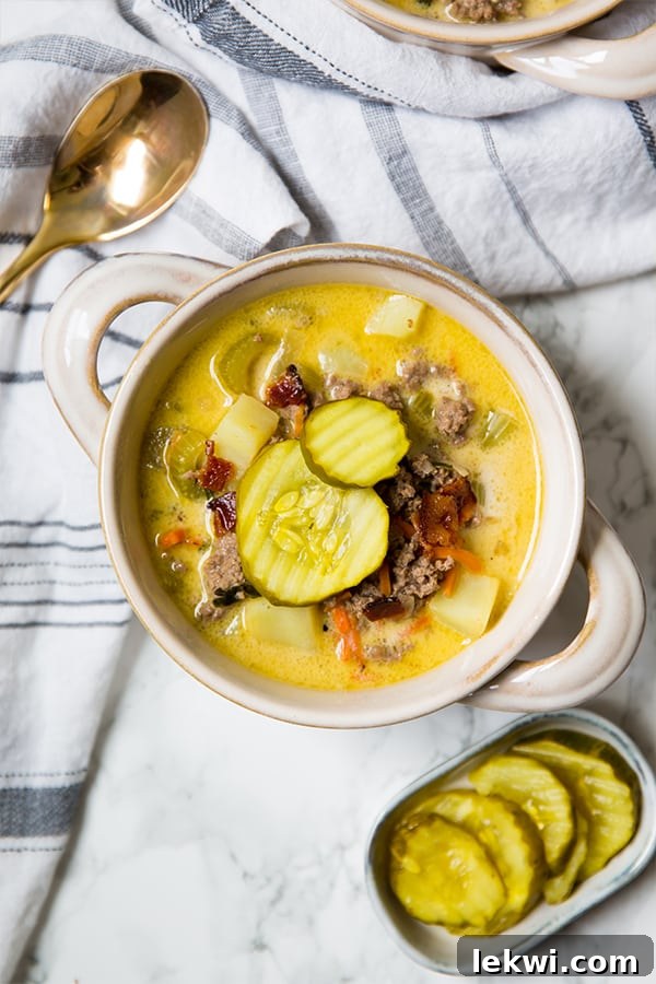 Paleo Bacon Cheeseburger Soup Creamy and Dairy Free 4 A hearty bowl of bacon cheeseburger soup, artfully topped with fresh pickles, rests on a rustic wooden surface, ready to be enjoyed.