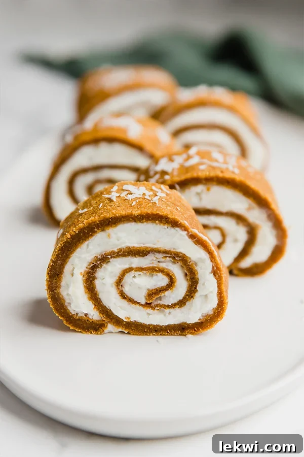 A beautifully arranged plate featuring several slices of a paleo pumpkin roll, dusted with a light powdered sweetener, set against a warm autumn backdrop.