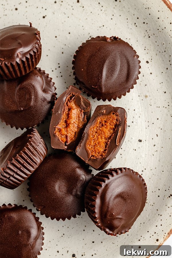 A speckled ceramic plate generously topped with a tempting array of chocolate pumpkin butter cups, showcasing their vibrant orange filling and rich chocolate coating, ready to be enjoyed.