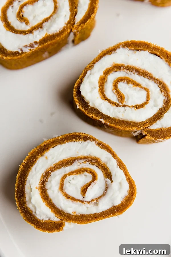 Exquisite slices of paleo pumpkin roll cake, featuring a beautiful swirl of creamy filling, neatly arranged on a kitchen counter, ready to be enjoyed.