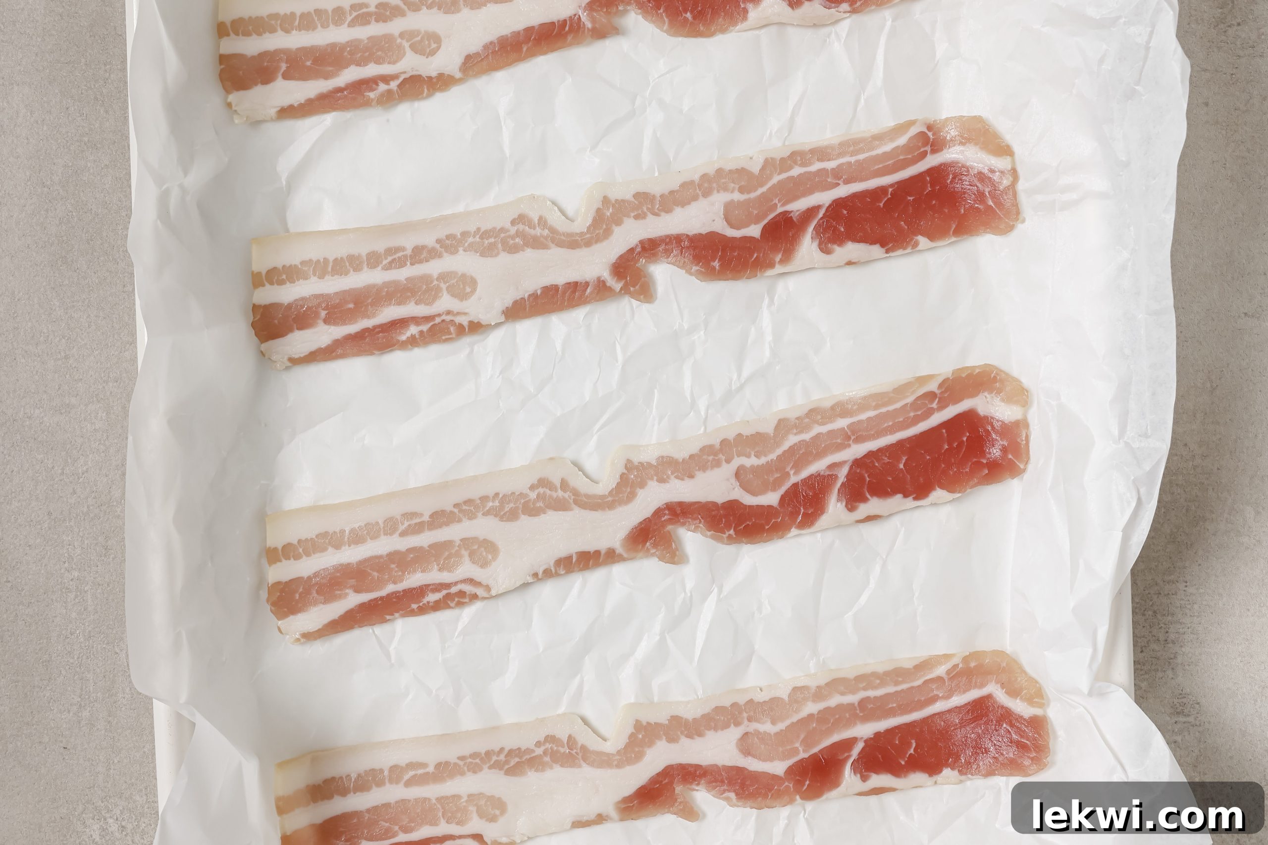 Uncooked bacon strips laid out on a parchment-lined baking sheet, ready for roasting.