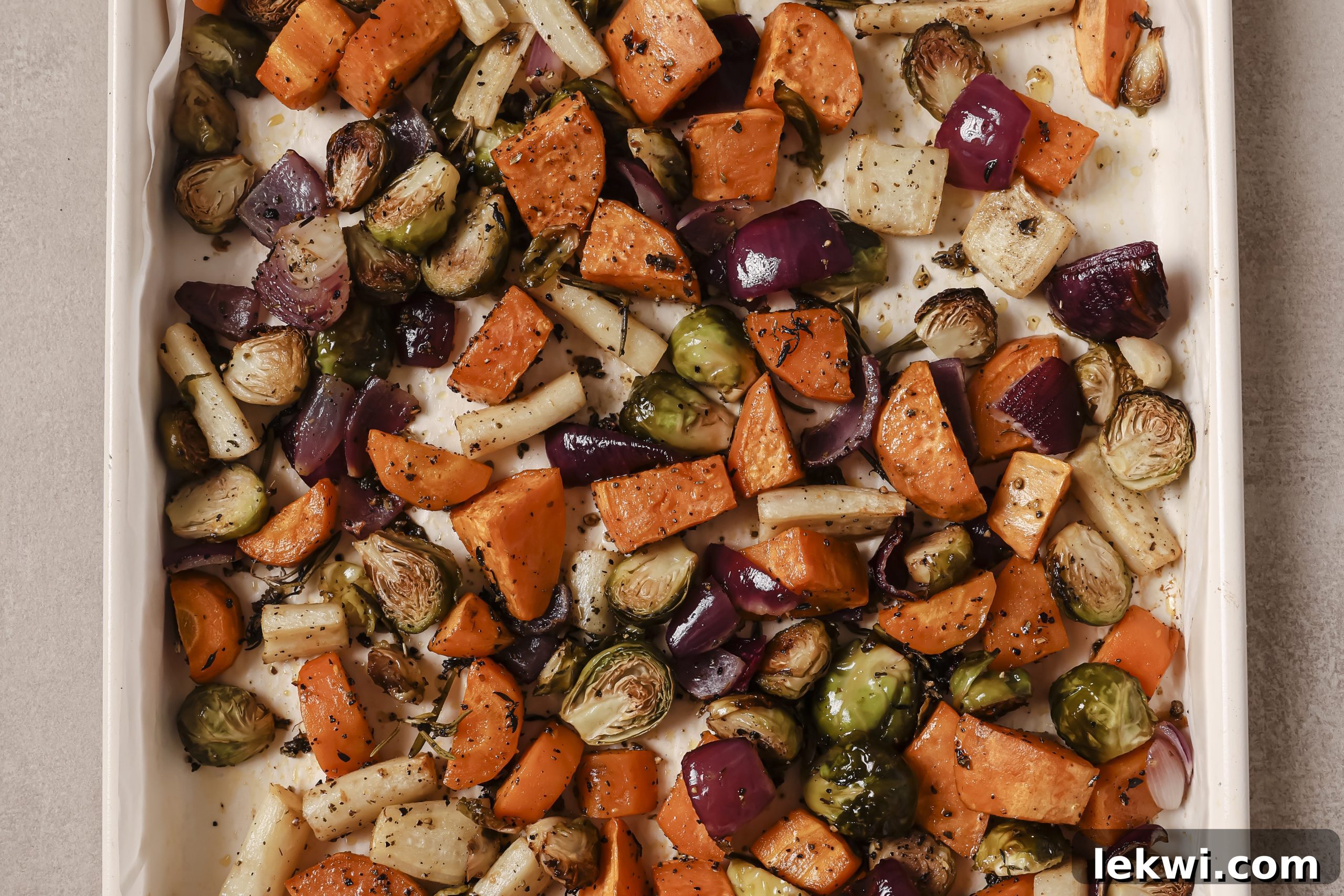 Fully roasted harvest vegetables including sweet potato, parsnip, Brussels sprouts, and red onion, golden brown and crisp on a baking sheet.