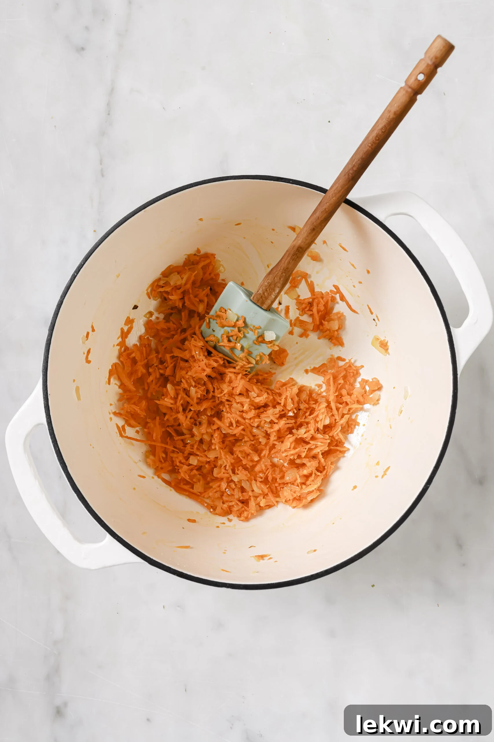 Shredded carrots being cooked in a white pot.