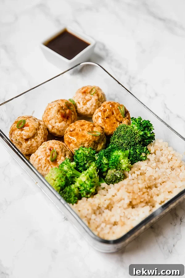 A glass meal prep container filled with teriyaki meatballs, broccoli, and cauliflower rice.
