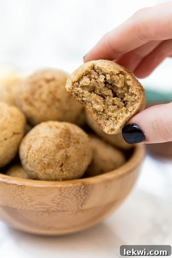 A hand taking an apple donut hole out of a wooden bowl filled with them.
