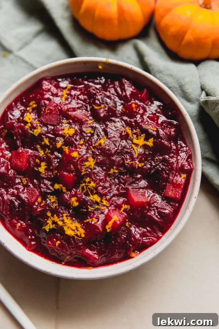 Vibrant Apple Cranberry Sauce in a serving bowl, garnished with fresh orange zest. This homemade sauce is perfect for Thanksgiving and offers a healthier, no-refined-sugar option.