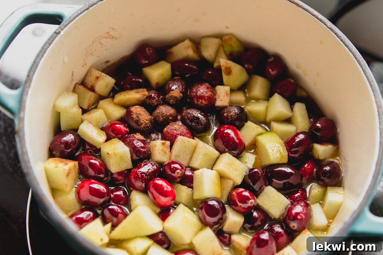 Fresh cranberries, diced apples, orange juice, and cinnamon combined in a blue pot, ready to be cooked.