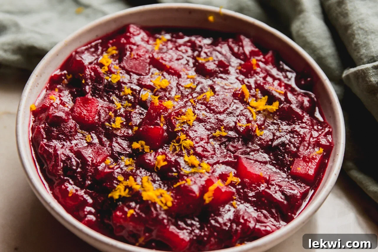 Chilled apple cranberry sauce in a white bowl, beautifully topped with vibrant orange zest.