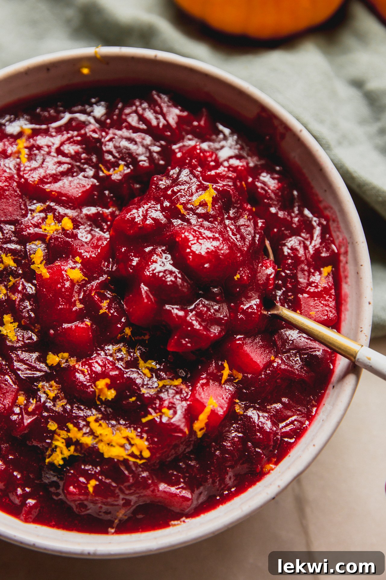 A close-up of apple cranberry sauce in a bowl with a spoon, highlighting its texture and freshness.