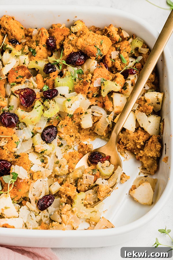 A close-up of a platter of golden brown cornbread stuffing with a serving spoon.