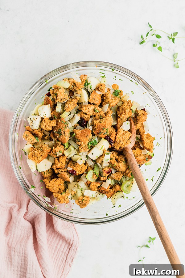 A mixing bowl filled with corn-free cornbread cubes, sautéed vegetables, dried cranberries, and herbs, ready to be tossed.